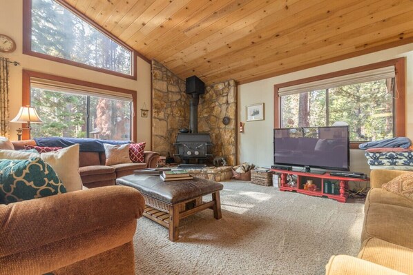 Open concept great room with vaulted ceilings / windows, large flat screen SmartTV, wood burning stove and sectional sofa.