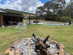 Outdoor entertainment area with large cover roof next to pool bbq trampoline and hot spa