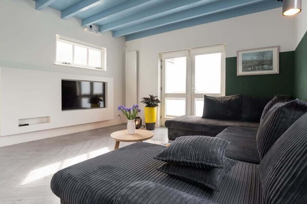 Bright and modern living room with comfy lounge sofa, smart TV and a playful touch of sky-blue ceiling — perfect for relaxing 
