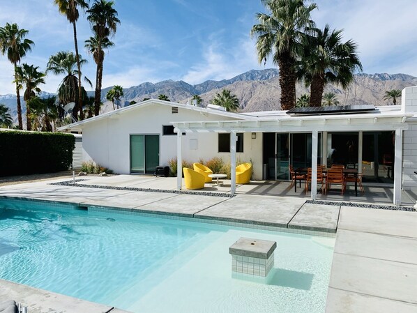 Large outdoor area with pool, spa and dining table.