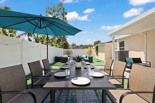 Step into this secluded backyard retreat, featuring a dining table for 8, a seating area for 6, and shaded spots with additional seating. Enjoy activities like mini golf and cornhole.