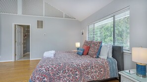 Comfortable sleeping space with light gray walls, hardwood floors, and a vaulted ceiling with decorative grates.
