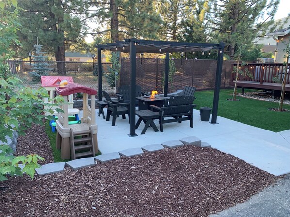 Fenced/landscaped front yard with fire pit, deck, BBQ, and toddle outdoor items.