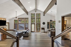 Living Room With Open Floor Plan Into Kitchen, Featuring Vaulted Ceiling and Large Windows.