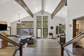 Living Room With Open Floor Plan Into Kitchen, Featuring Vaulted Ceiling and Large Windows.