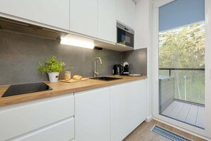 A sleek, modern kitchen with light-colored cabinets, stainless steel appliances, and a window looking out onto a green area.