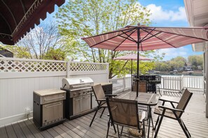 Outdoor deck with a BBQ grill station and ample seating under large umbrellas, offering a perfect spot for al fresco dining with serene lake views.