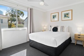 The primary bedroom features a comfortable queen-size bed with a cosy pile of throw pillows, warm side lamps and block-out curtains.
