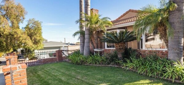 The front yard has an abundance of green grass and queen palm trees