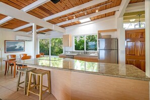 Modern kitchen oasis. Spacious and framed by greenery, boasting a marble island, wooden accents, and abundant natural light.