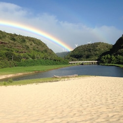 A serene landscape under a vibrant rainbow, where lush valleys meet calm waters and sandy shores.