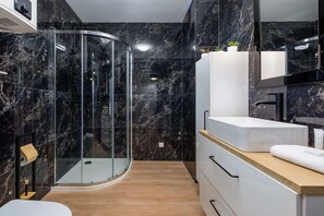A modern bathroom with dark, marble-like walls and a glass shower enclosure. The space looks elegant and luxurious.
