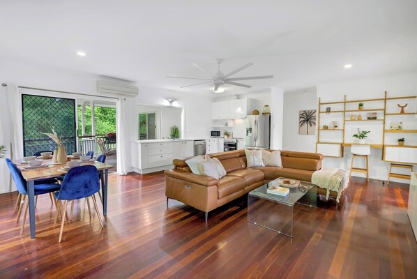 Step into the spacious living room featuring plush leather sofas, a central TV, and abundant natural light.