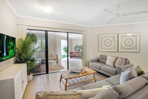 Relax in the stylishly furnished living room, featuring comfortable sofas and a central TV—perfect for unwinding after a day of exploring or lounging by the shared pool.