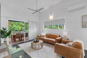 A bright and airy living room houses modern furnishings, offering a seamless connection to the outdoor balcony surrounded by lush greenery.