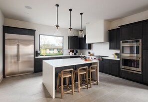 (1st Floor) Fully equipped kitchen with stainless steel appliances, cooking essentials, and kitchen island bar seating.