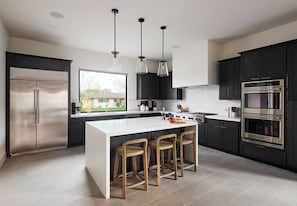 (1st Floor) Fully equipped kitchen with stainless steel appliances, cooking essentials, and kitchen island bar seating.