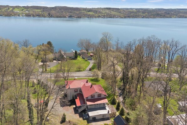 Stunning aerial view of a red-roofed home nestled in lush greenery, offering direct access to the serene lakefront—perfect for tranquil living or vacation getaways.