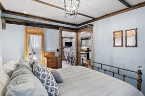 Charming bedroom featuring exposed wooden beams and a rustic metal bed frame, with a soothing blue palette that extends seamlessly into a modern kitchen area, perfect for a relaxing and convenient stay.