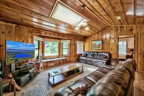 Cozy living room with knotty pine walls, rock wood burning fireplace, large flat screen TV and leather sofas.