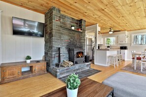Cozy living room on the main floor, featuring a smart TV and a wood-burning fireplace in front the large U-shaped sofa. At the back, the dining area with seating for six, and additional space at the counter next to it.