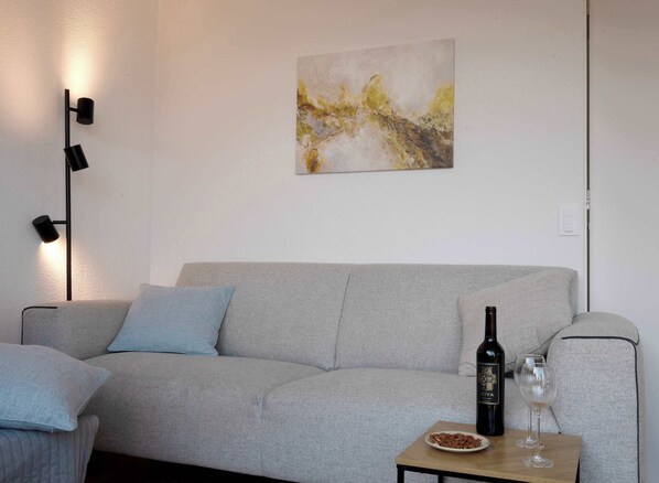 Modern lounge area with cozy touches
Relax with a glass of wine in this bright, inviting space featuring a soft sofa, elegant lighting, and serene artwork.
