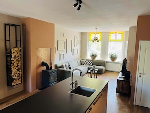 A bright and stylish open-plan living room with a cozy wood stove, kitchen island, and large windows that bring in lots of natural light.