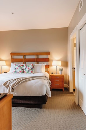 Relax in this serene bedroom, featuring warm neutral tones, a wooden slat headboard, and crisp white linens. Floral pillows add a touch of charm, while the en-suite bathroom offers added convenience.