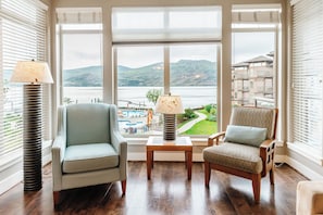 Enjoy stunning water and mountain views from this modern sitting area, featuring two cozy armchairs, a side table, and warm lighting. The dark hardwood floors and neutral tones create an elegant, serene space.