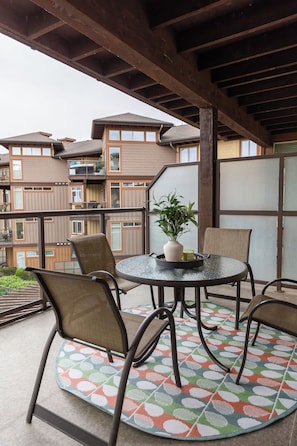 Unwind on this charming balcony with a round glass-top table and comfy wicker chairs. A vibrant patterned rug and potted plant add warmth, while the frosted glass partition ensures privacy.