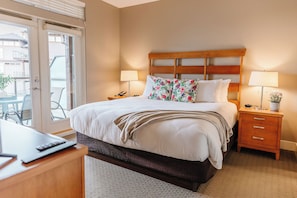 Relax in the inviting bedroom, featuring a king-sized bed with crisp white linens, a wooden headboard, and matching nightstands. Enjoy working at the desk or step out onto the balcony for fresh air.