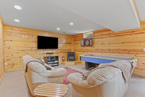 Cozy game room featuring fireplace, Smart 65 InTV, airhocky, dart board.