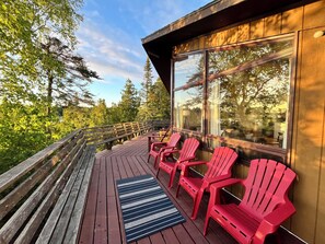  A spacious deck featuring four red Adirondack chairs, perfect for relaxing and enjoying the surrounding nature and beautiful sunset views.