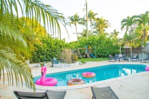 Escape to your private tropical oasis! Relax by the large pool surrounded by lush greenery, with cozy lounge chairs and fun inflatables. Plus, a children's playset ensures family fun for all ages. Perfect for a serene getaway!