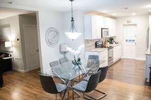 Bright and modern dining area with a sleek glass table that seats 6, flowing seamlessly into a fully equipped kitchen featuring stainless steel appliances, ample counter space, and stylish cabinetry. Perfect for enjoying meals and cooking together.