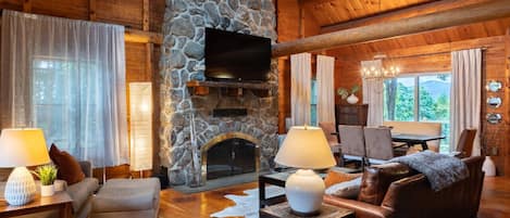 Cozy up in our charming log cabin in Gilford, NH—where rustic charm meets modern comfort. The main living space has an open floor plan, featuring a large leather couch, chair and a half, and dining area that overlooks the yard with views of Gunstock Mount