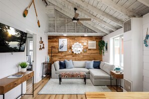 Relax in our cozy living room: a plush sofa anchors the space against a chic wooden wall adorned with modern decor, basking in soothing natural light. Embrace comfort and style in every corner.