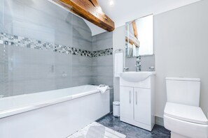 En-suite bathroom with exposed beams and a bath with overhead shower attachment
