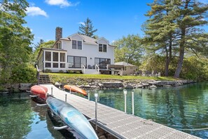 The Lakehouse from the large dock with kayaks and canoe, covered veranda, uncovered built-in seating, gas firepit and wood-burning firepit below