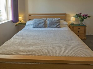 Double bed with blanket and pillows, bedside cabinet and lamps and a vase of flowers