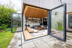 Spacious living room with expansive windows wide open, bringing the outdoors in and offering a seamless view of the garden