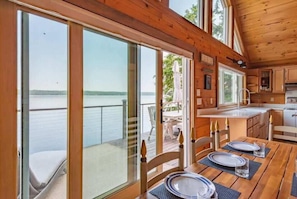 **Dining Area with Lake View**: "Dine with a view in our cozy dining area, featuring large windows and doors that open directly to the deck overlooking the tranquil lake.