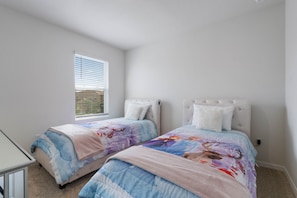 Cozy kids’ room with twin beds, soft carpeting, and cheerful themed bedding.
