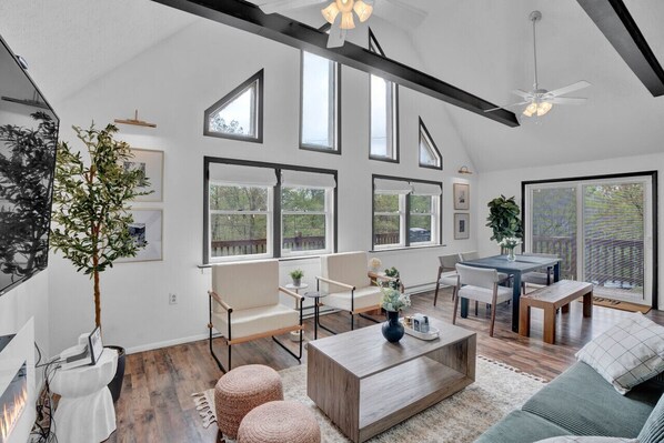 Bright living area with high ceilings and large windows, providing plenty of natural light. Features comfortable seating, a dining area, and modern decor. Opens to a spacious deck with scenic views. Ideal for relaxation and entertaining.