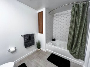 Relax and refresh in our well-appointed bathroom featuring a bathtub, blowdryer, and complimentary essentials like toothpaste, towels, lotion, shampoo, conditioner, body wash, and hand soap.