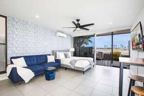 A serene and stylish coastal retreat featuring a modern open-plan living space with a cozy blue sofa, a comfortable bed, and a stunning ocean view from the balcony.