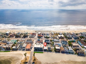A breathtaking aerial view of a coastal community showcasing a highlighted beachfront property. Nestled between the expansive ocean and a serene bay, this location offers unparalleled access to both beach and bay activities, providing a perfect setting fo