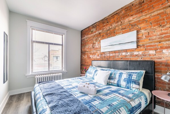 King Bed With Vibrant Blue Linens And A Stunning Exposed Brick Accent Wall
