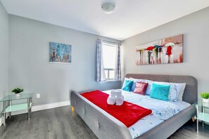 Spacious Bedroom With A King-Sized Bed, Bright Artwork, And Large Windows