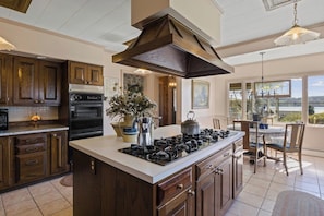 Inviting kitchen space highlighted by a prominent wooden cooking hood and island setup, flanked by deep-toned cabinetry and equipped with modern appliances, offering a functional yet cozy area for meal preparation and dining.